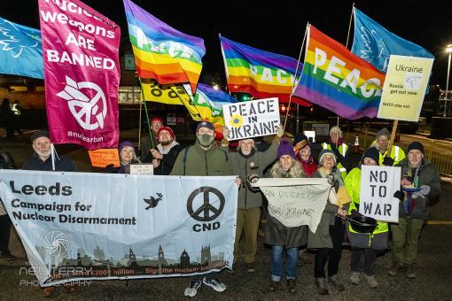 night time protest with peace flags flying and placard saying no to war